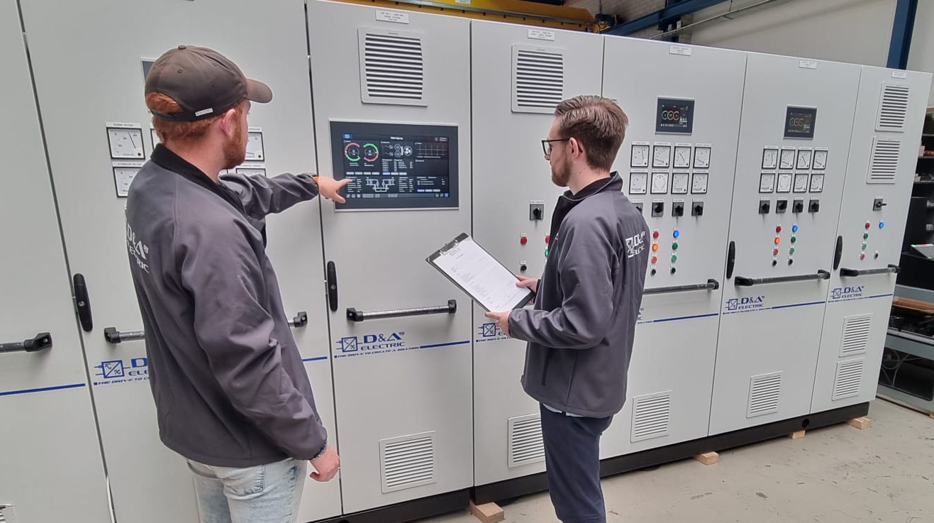 Twee collega's van D&A Electric testen de HMI van een hoofdschakelbord in de werkplaats in Ridderkerk